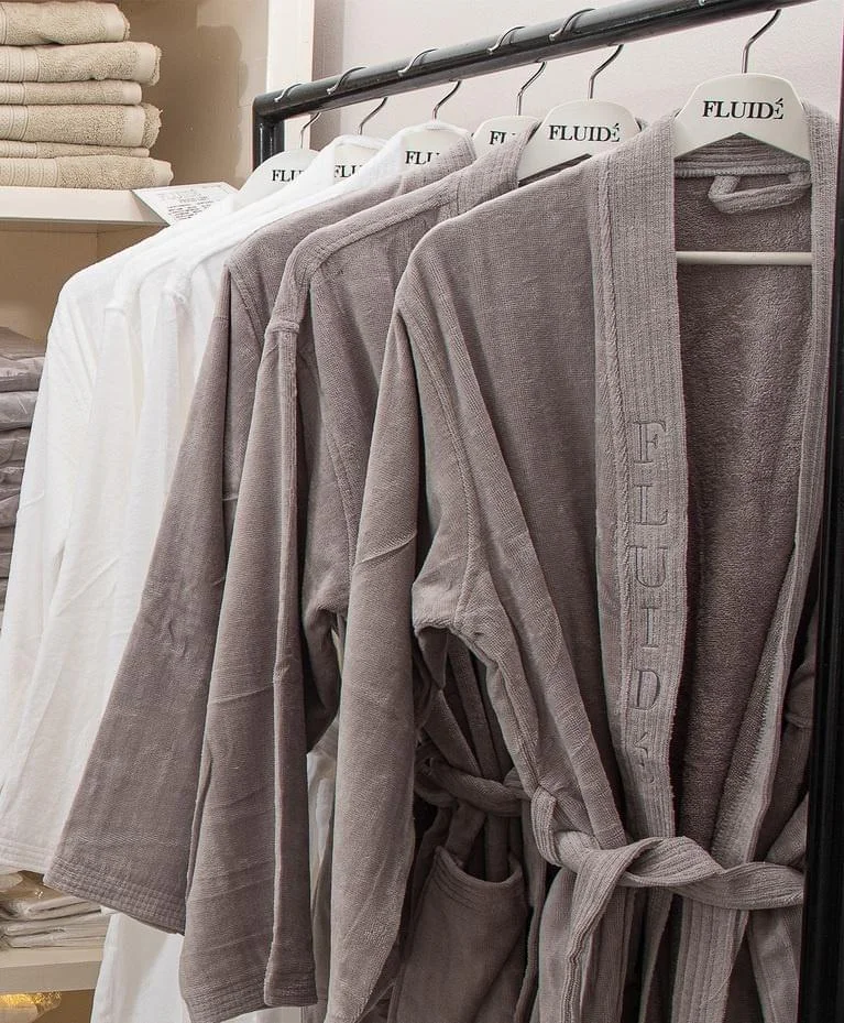 Lucca bathrobe in soft absorbent cotton, with long sleeves, side pockets, and tie belt, available in white, grey, beige, black, and brown.